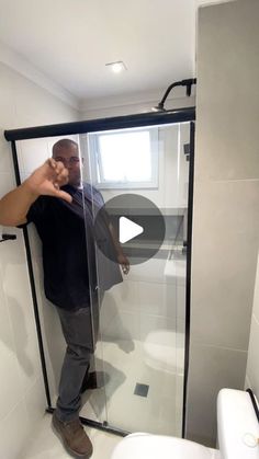 a man standing in a shower next to a white toilet and black framed glass door