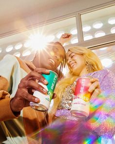 two people standing next to each other and holding drinks in their hands, with the sun shining behind them