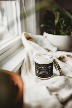 a candle sitting on top of a white towel next to a potted plant in a window sill