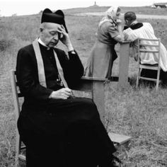 an old man sitting on a bench in a field with other people standing around him