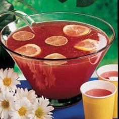 there is a bowl of fruit punch with lemons in it and two cups next to it