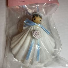 a small doll in a plastic bag on a white tablecloth with a blue ribbon around it's neck