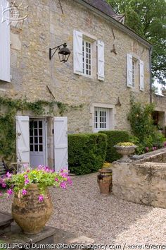 an old stone house with white shutters and flowers