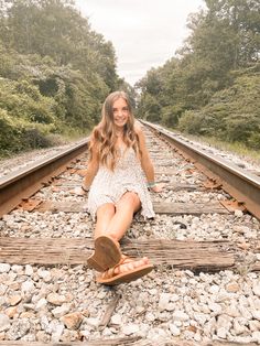 a woman sitting on the railroad tracks with her feet propped up and smiling at the camera