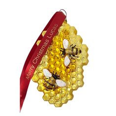 two bees are sitting on top of a honeycomb ornament with a red ribbon