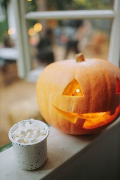 a carved pumpkin sitting on top of a window sill next to a cup filled with marshmallows