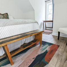 a bed sitting in the middle of a bedroom next to a white chair and window