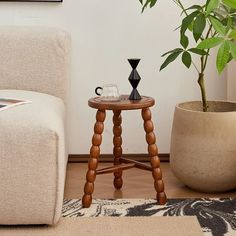 a small wooden table sitting next to a white chair and potted plant in a living room