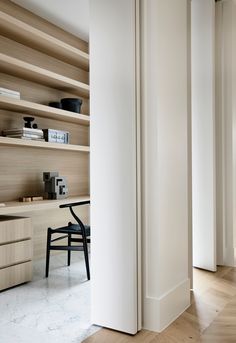 an office with white walls and wooden shelves on the wall, along with a black chair