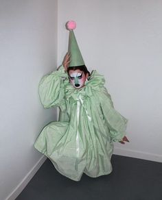 a person in a clown mask and green dress with a pink ball on their head