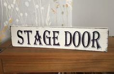 a wooden sign that says stage door sitting on top of a table next to a window