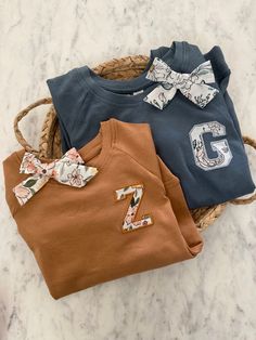 three baby clothes sitting in a basket on a marble counter top with the number two printed on it