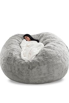 a woman wrapped in a blanket is laying on a large grey bean bag chair with white fur