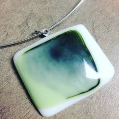 a green and white square shaped pendant on a silver necklace with a black circle in the center