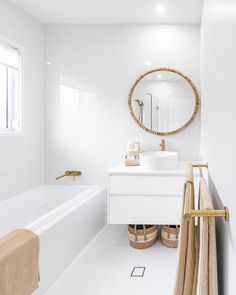 a bathroom with white walls and flooring has a large round mirror above the sink