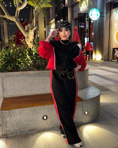 a woman is standing on the sidewalk in a black and red outfit