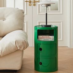 a green trash can sitting on top of a hard wood floor next to a white couch