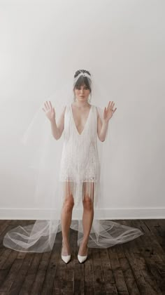 a woman in a white dress and veil standing on a wooden floor with her hands up