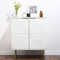 a white cabinet sitting on top of a wooden floor next to a vase with flowers