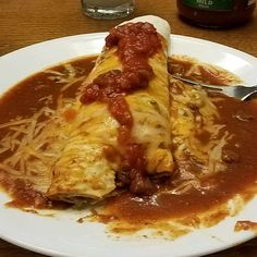 a white plate topped with enchilada covered in sauce