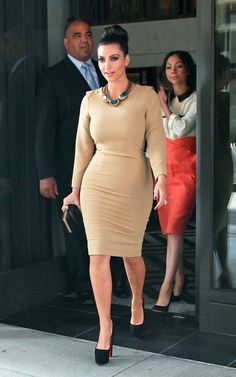 a woman in a tan dress is walking out of a building with her hand on her hip