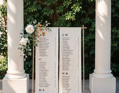 two white columns with flowers and names on them for an outdoor wedding ceremony in front of some greenery