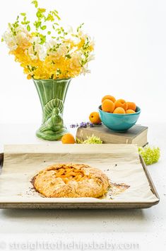 there is a pie on the tray next to some oranges and flowers in a vase