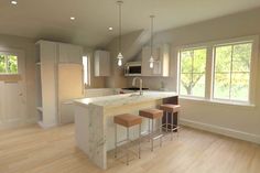 an empty kitchen with two stools in front of the island and windows on both sides