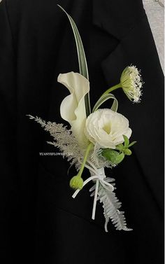 a boutonniere with white flowers and greenery on the lapel of a suit