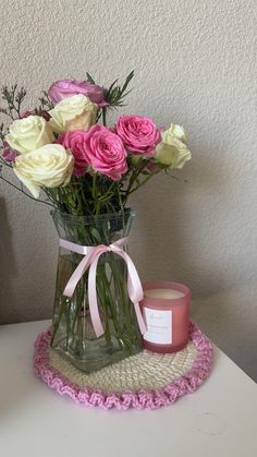 pink and white roses in a glass vase on a table with a candle next to it