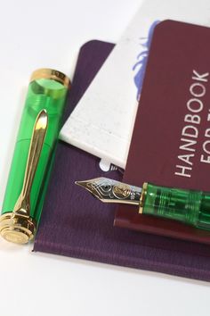 a green fountain pen sitting on top of a purple book