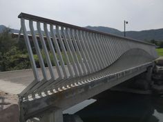 a bridge over a body of water with mountains in the background and grass on either side