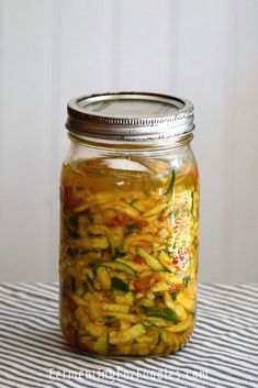 a glass jar filled with pickled vegetables on top of a striped table cloth next to a white wall