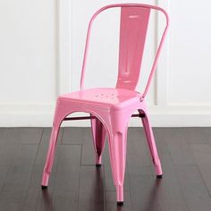 a pink chair sitting on top of a hard wood floor next to a white wall