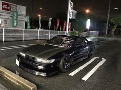 a black car parked in front of a gas station at night with its lights on