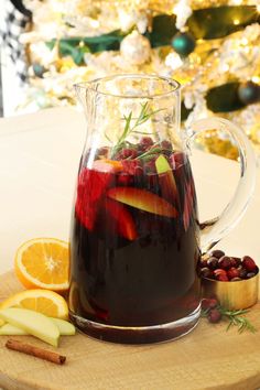 a pitcher filled with liquid sitting on top of a cutting board next to sliced apples and cranberries