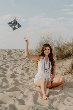 a woman sitting in the sand with her hand up and a kite flying above her head