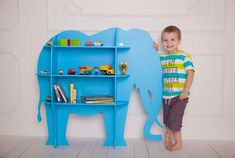 a little boy standing next to a blue shelf with a toy elephant on top of it