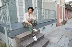 a woman sitting on the steps talking on her cell phone while wearing camo pants