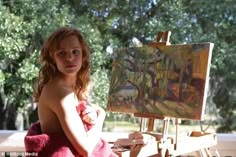 a naked woman sitting in front of an easel with a painting on the table