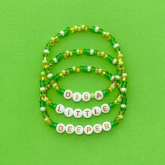 three green and white beaded bracelets with name beads on each strand, sitting on a green surface