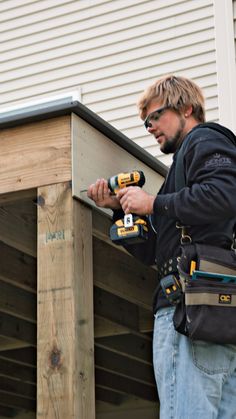 a man holding two drillers on top of a wooden deck next to a building