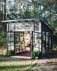 a small greenhouse with lots of windows and plants in the front door, sitting on grass