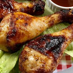 two pieces of chicken sitting on top of lettuce next to a bowl of sauce