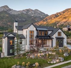 a large white house with black roof and windows in front of the mountain range at sunset