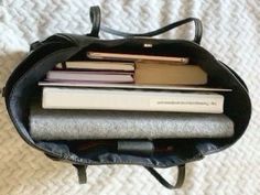 an open book bag sitting on top of a bed with several books in the back