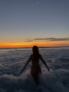 a woman standing in the ocean at sunset