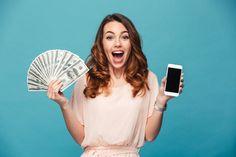 a woman holding a cell phone and money in one hand while standing against a blue background