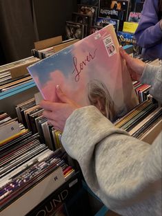 a person is holding up a record in front of a pile of cd's