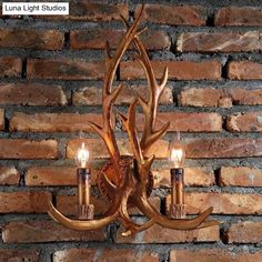 an antler chandelier with two candles on it in front of a brick wall